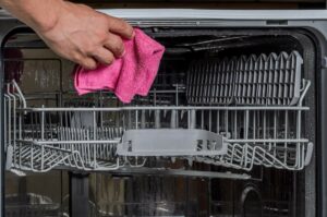 hand with pink cleaning rag cleaning interior of dishwasher