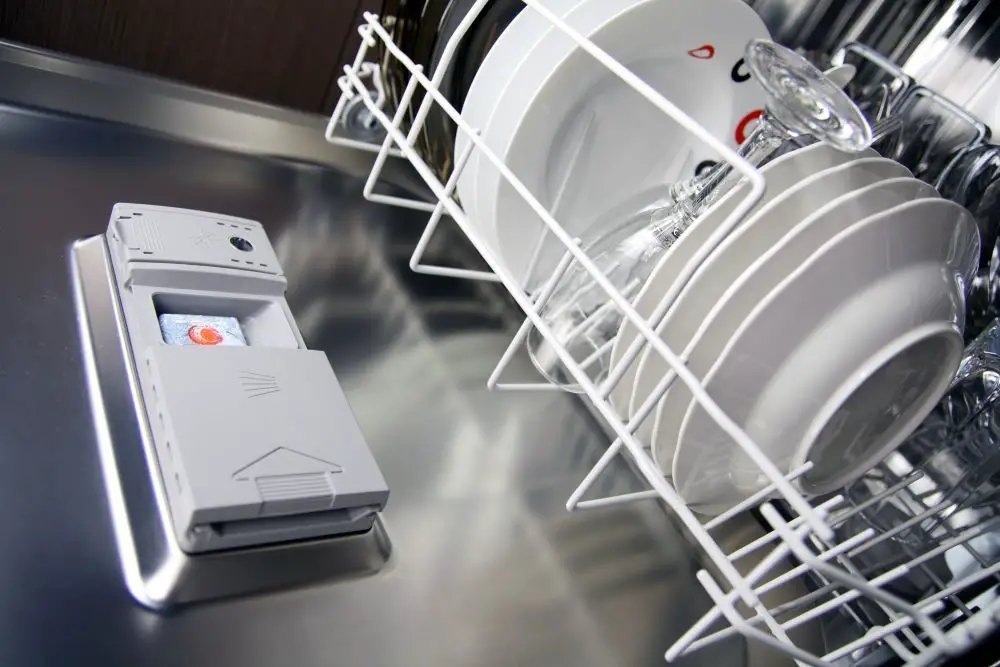 detergent in a open dishwasher with some plates and a glas